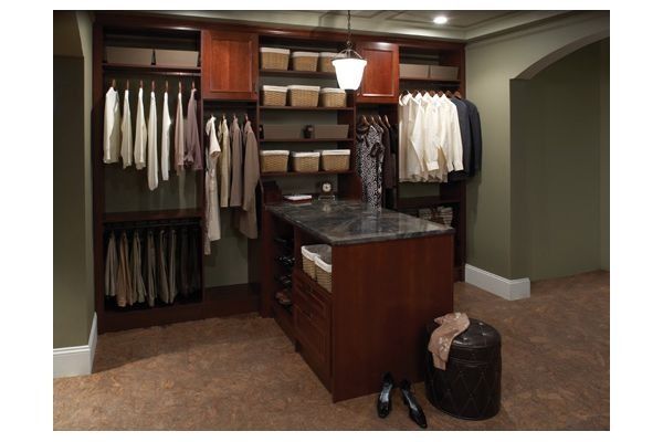 Walk-in closet with dark wood shelving, hanging clothes, and an island with storage. Olive green walls.
