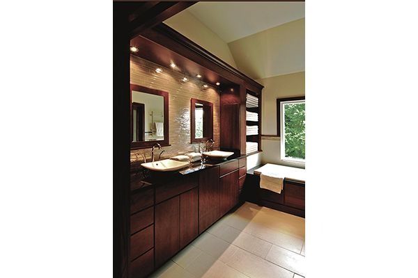 Bathroom with dark wood vanity, mirrors, and lighting, next to a window with a bathtub and towels.