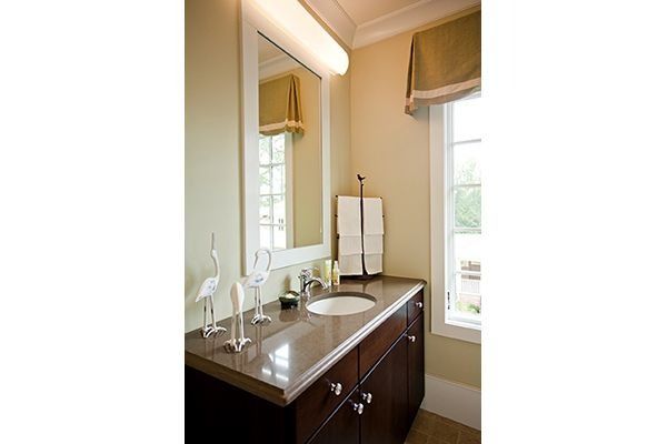 Bathroom with dark wood vanity, light countertop, mirror, and window with beige walls.