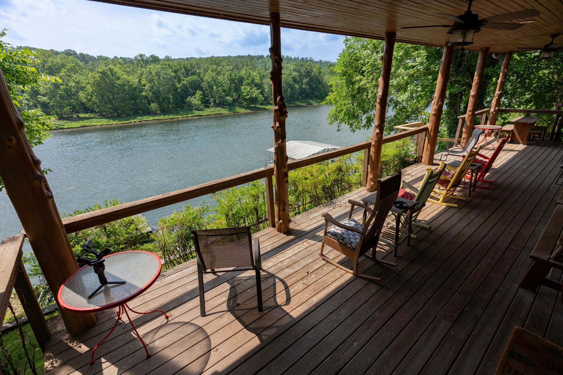 Covered riverside deck with chairs and tables overlooking a calm river and green trees