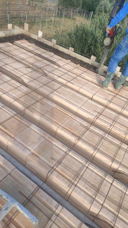 Cantiere edile con griglia di barre d'armatura su casseratura in legno e un operaio in piedi sul bordo.