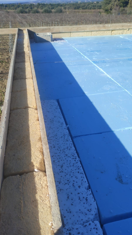 Pannelli solari blu accanto a una parete di cemento sul tetto, con un paesaggio aperto sullo sfondo.