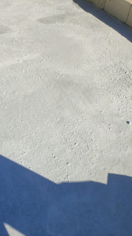 Superficie di cemento bianco illuminata dal sole accanto a un bordo dipinto di blu e a una parete color beige.