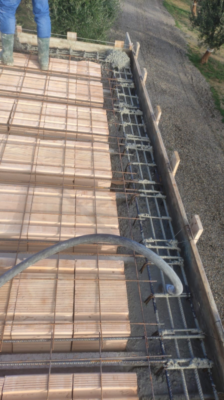 Armature in ferro e casseforme in legno per una soletta in cemento armato a lato di un sentiero pavimentato.