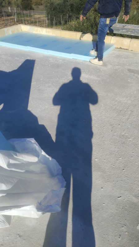 Un vialetto lastricato con lunghe ombre, una persona in piedi vicino a un marciapiede dipinto di blu e materiali bianchi in primo piano.