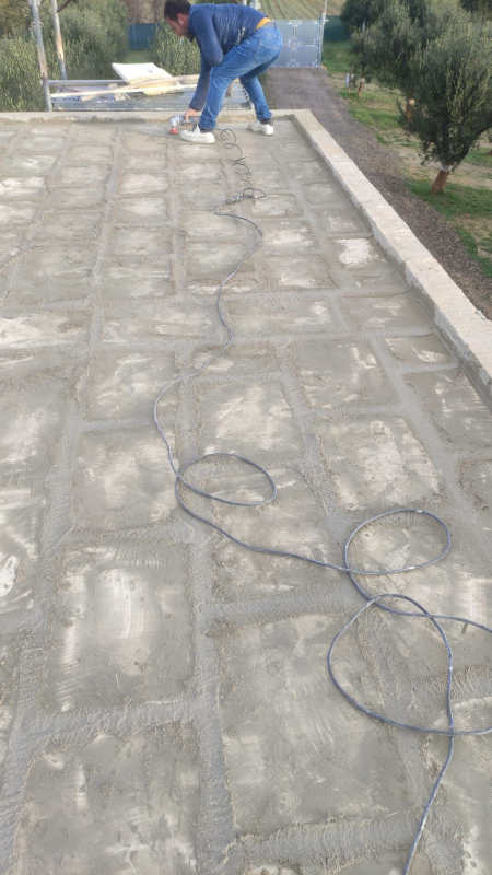 Un operaio in divisa blu sta riparando un vialetto in pietra con dei cavi tesi sul pavimento.