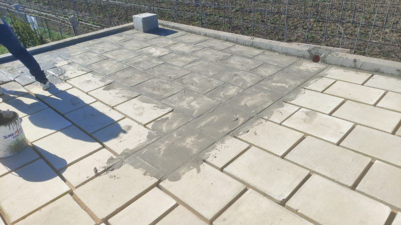 Gambe di persona su un tetto di tegole con una zona grigia di pavimentazione riparata e una piccola presa d'aria.