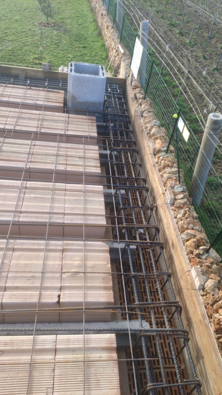 Armature in ferro e casseforme in legno per una soletta in cemento armato accanto a una recinzione metallica e a un bordo erboso.