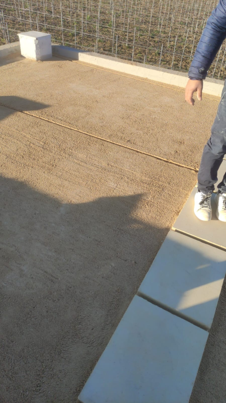 Passerella esterna in cemento accanto a una recinzione, con una persona in piedi sul bordo e la sua ombra proiettata sul terreno.