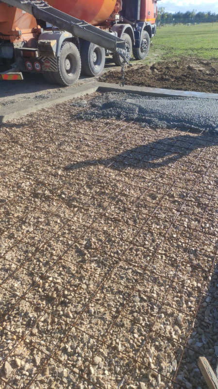 Camion da cantiere arancione che sparge ghiaia sulla banchina stradale accanto a un campo di terra