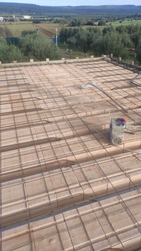 Tettoia in cemento armato con griglia di barre d'armatura, vista dall'alto con colline boscose sullo sfondo.