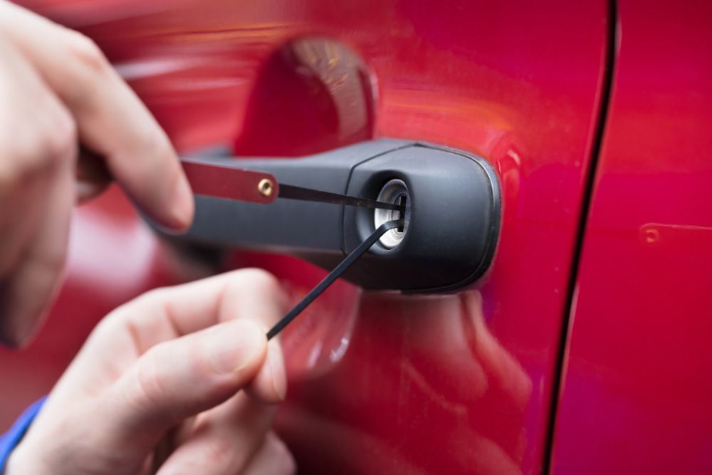 Locksmith using pick tools to open a car door lock on a red vehicle.