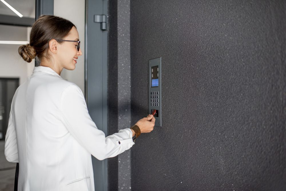 A woman in a white jacket is pressing a button on a wall — Locksmith in Helensvale, QLD