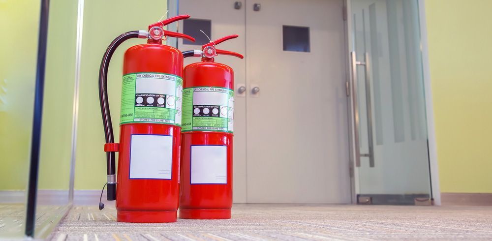 Two red fire extinguishers are sitting on the floor in front of a door — Locksmith in Tweed Heads, NSW