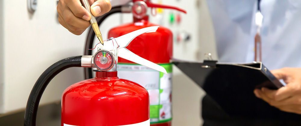 Person is checking a fire extinguisher while holding a clipboard — Locksmith in Tweed Heads, NSW