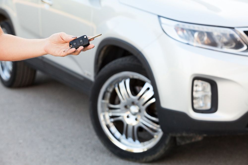 A person is holding a car key in front of a white car — Locksmith in Surfers Paradise, QLD