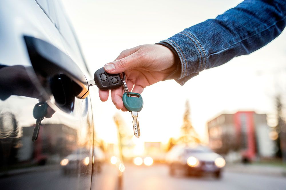 A person is holding a car key in front of a car — Locksmith in Currumbin, QLD
