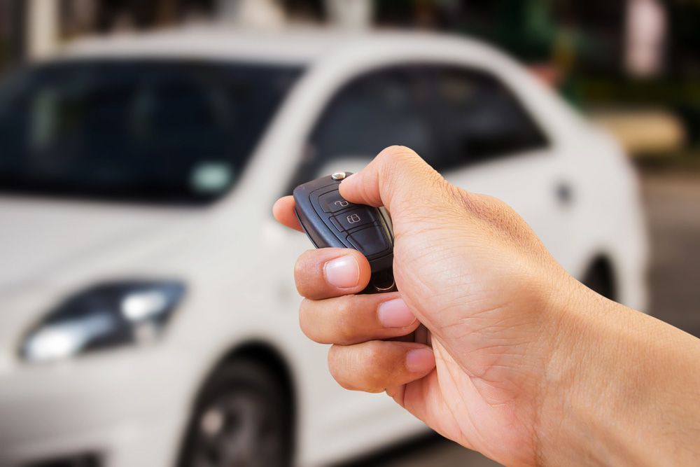 A person is holding a remote control in front of a white car
