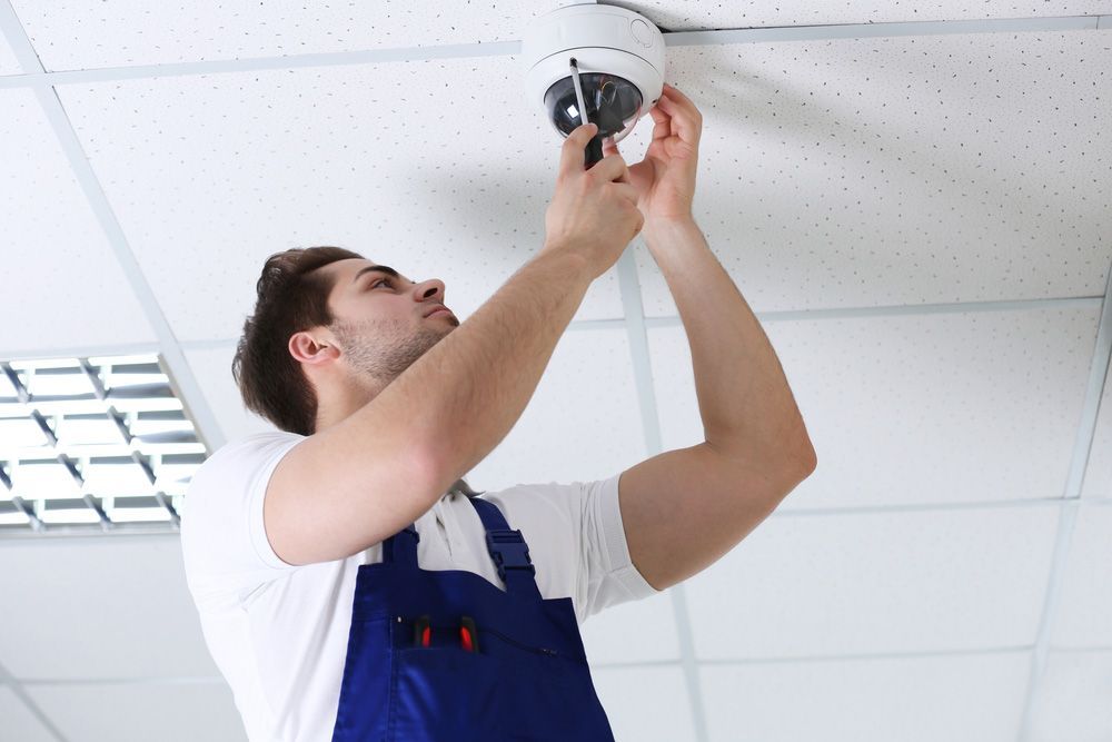 A man in blue overalls is installing a security camera on the ceiling — Locksmith in Tweed Heads, NSW