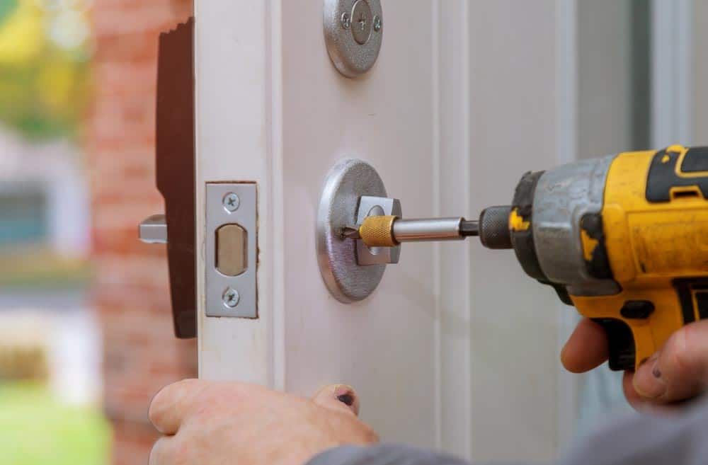 A Person Is Installing Door Lock With A Drill — Border Locksmiths & Electronics In Tweed Heads, NSW