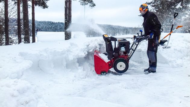 En man använder en snöslunga för att röja snö från en uppfart.