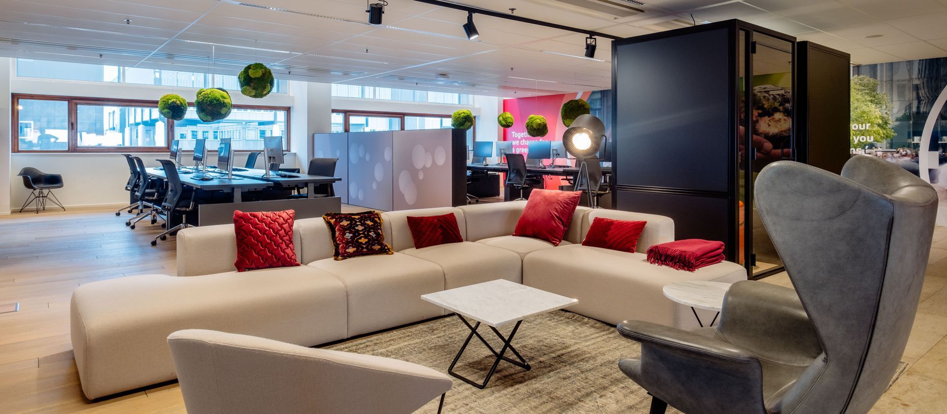 Bright modern office lounge with white sofa, red pillows, chairs, and open workspace area