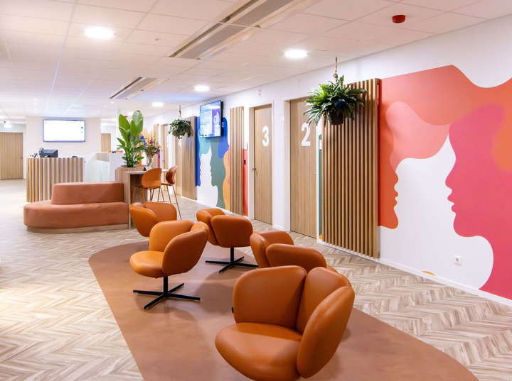 Moderne wachtruimte met oranje stoelen, beige banken, potplanten en genummerde privécabines.