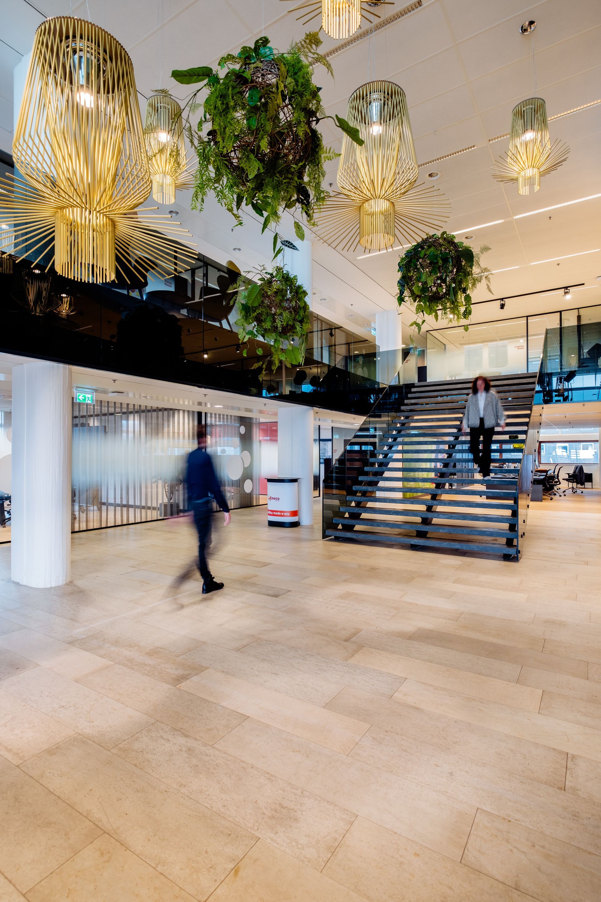 Lichte kantoorlobby met hangplanten, gouden hanglampen en een houten trap van Eneco eMobility in Rotterdam, interieurontwerp door KuóStudio