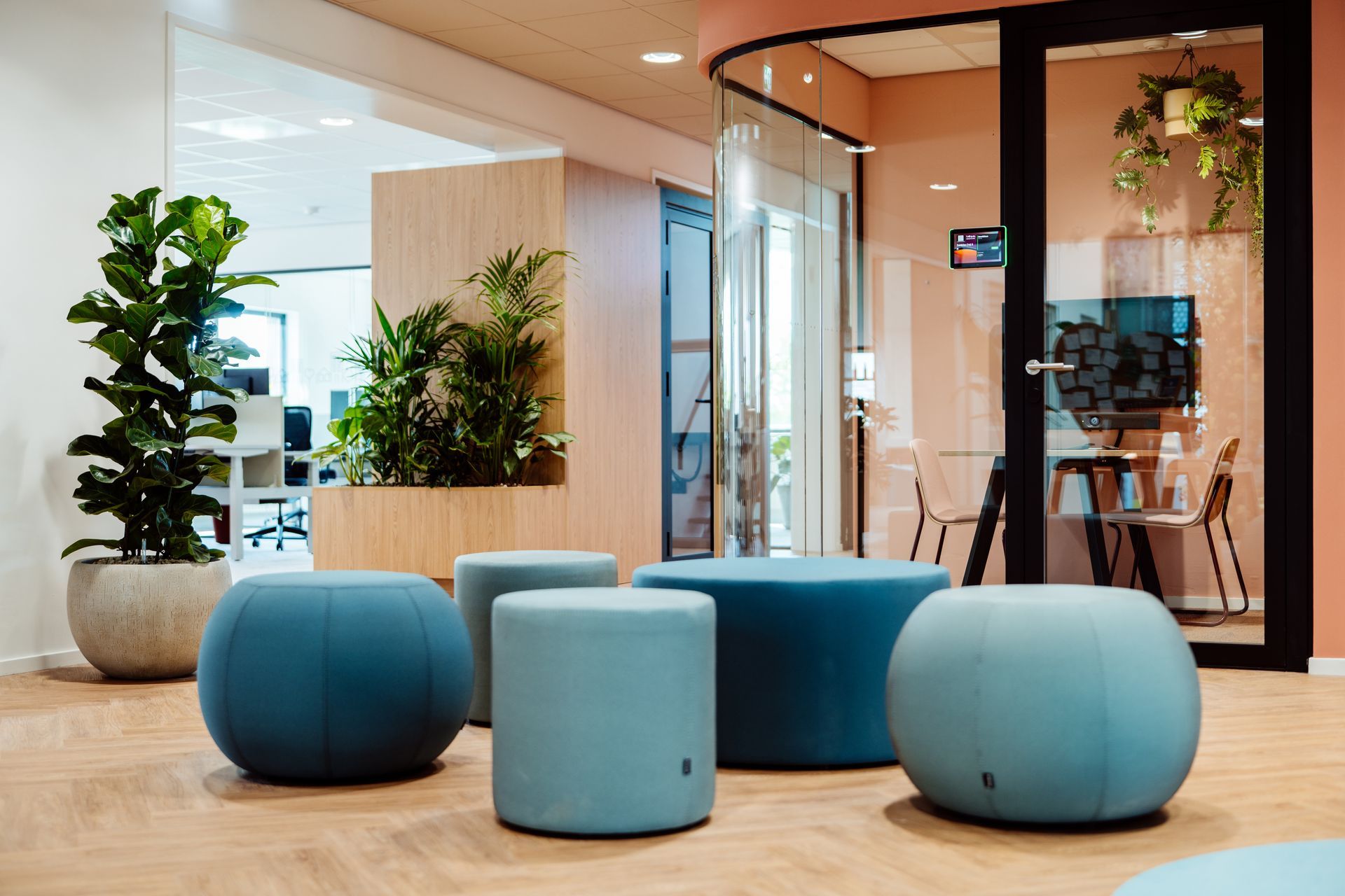 Moderne kantoorlounge met blauwe ronde krukken, potplanten en glazen vergaderruimtes interieurontwerp door KuóStudio