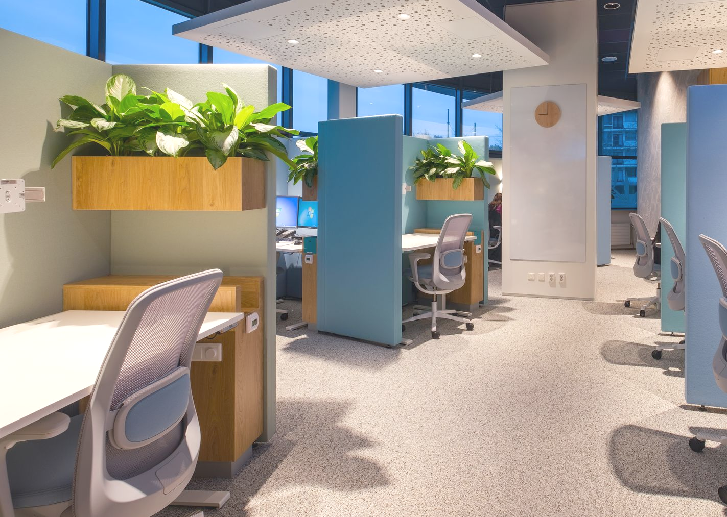 Moderne kantoorruimte met blauwe cubicles, houten lambrisering, bureaus, stoelen en een roze zithoek met banken in Rijswijk