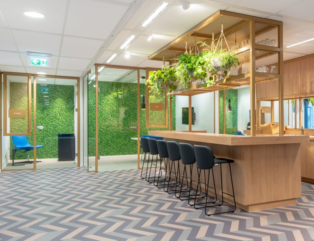Moderne kantoorlounge met barzitjes, houten accenten, hangplanten en groene afscheidingswanden in Rijswijk.