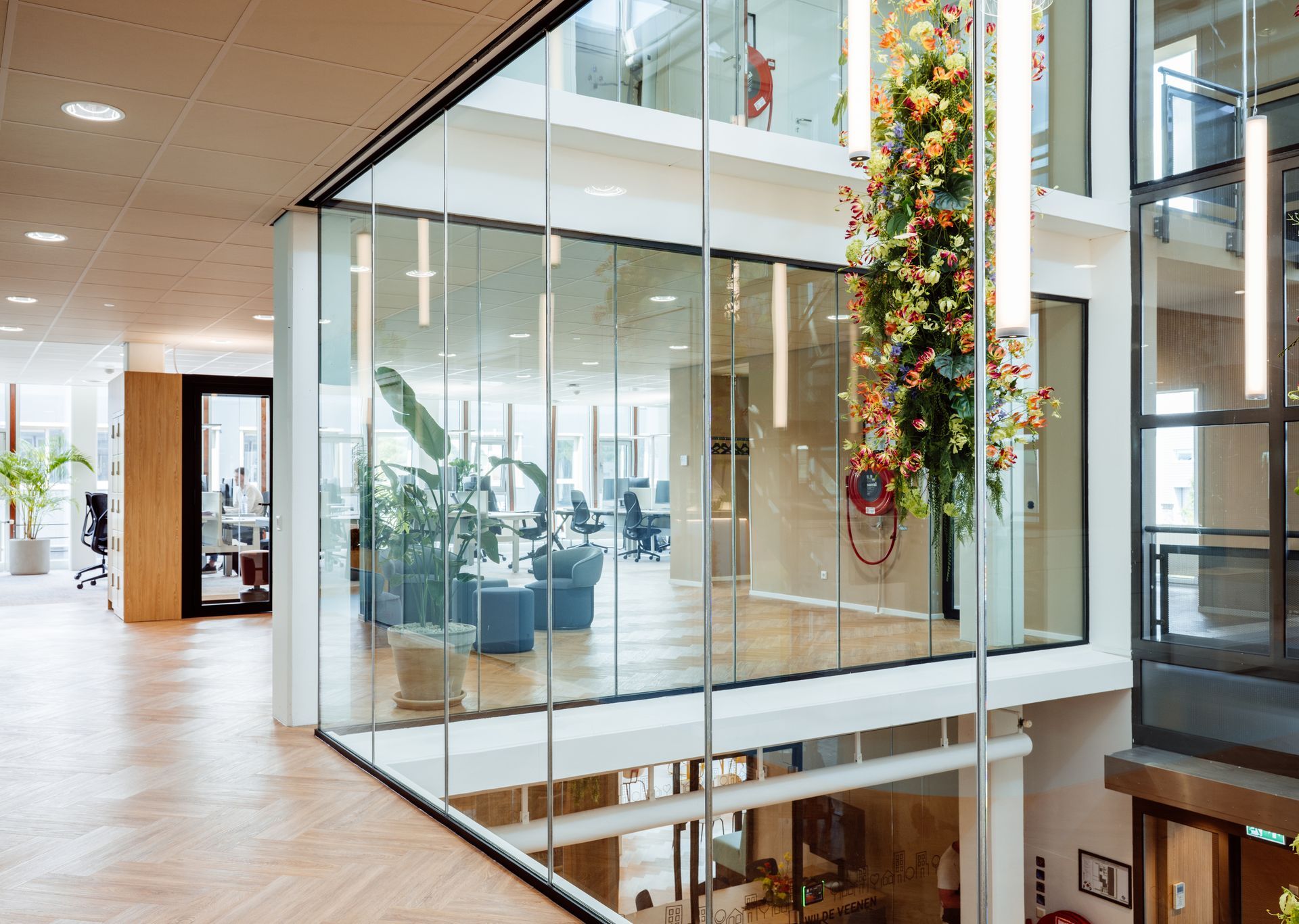 Na verbouwing Modern glazen kantooratrium met een hoge, bloemrijke versiering en zitgelegenheid achter glazen wanden. interieurontwerp door KuóStudio
