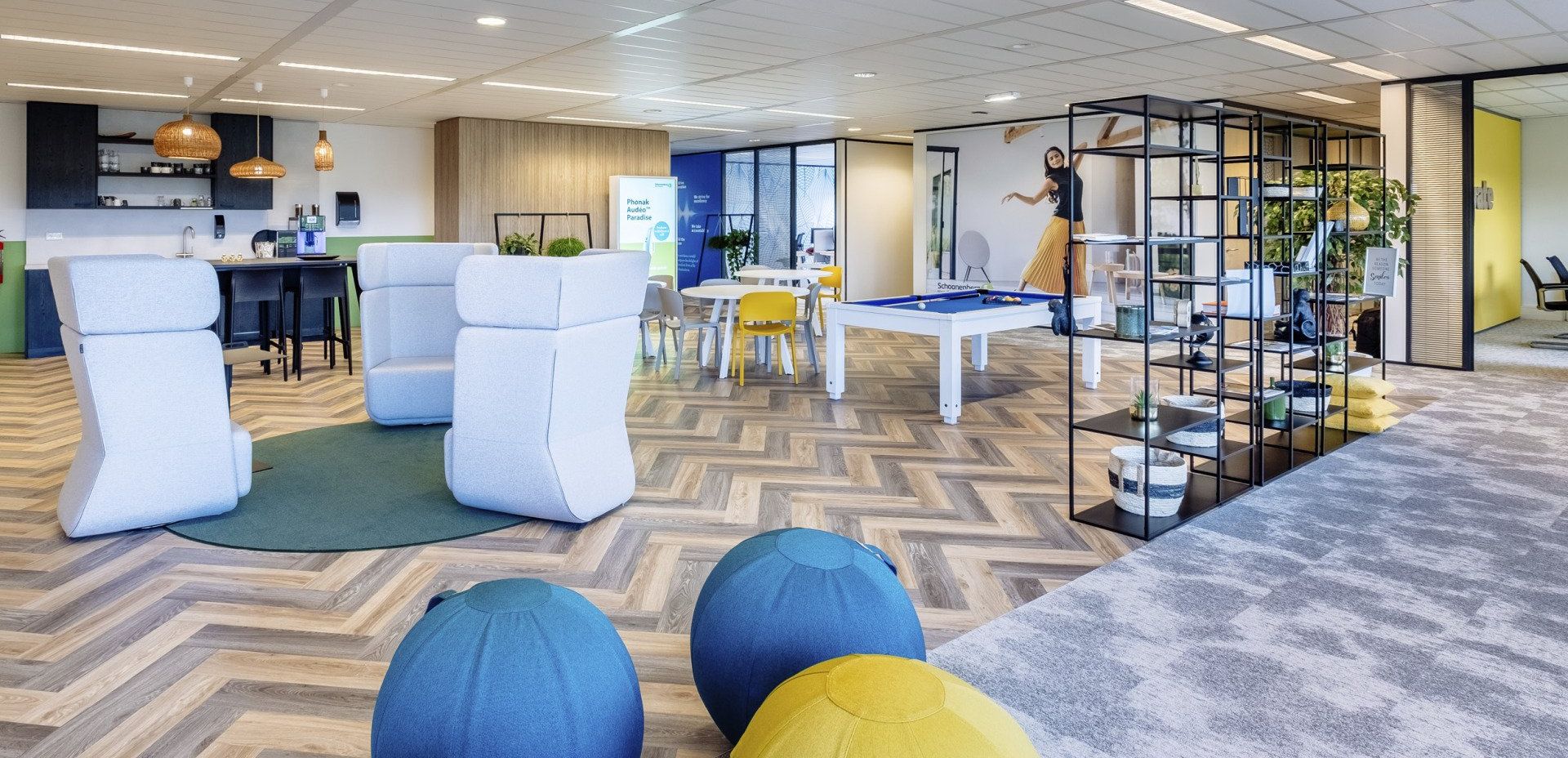 Moderne lounge met witte stoelen, blauwe poefs, een chevronkleed en zwarte planken in een lichte, open kantoorruimte in Rotterdam