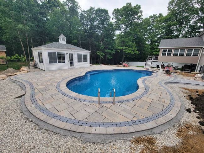 A large swimming pool is surrounded by trees and a wooden deck.