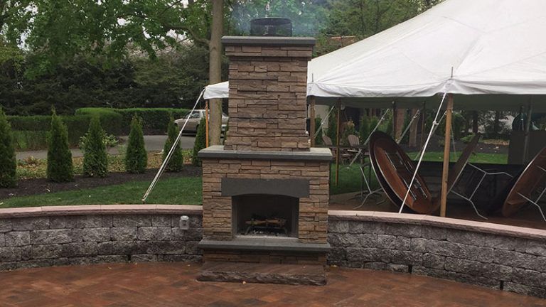 A brick fireplace is sitting on a brick patio next to a white tent.