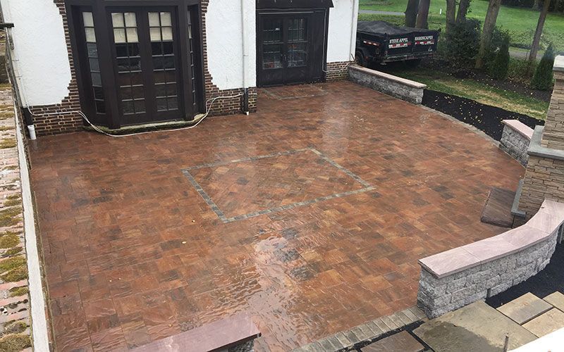 A brick patio with a bench in front of a house.