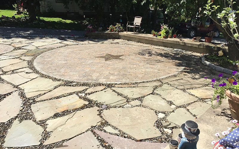 A statue of a man in a top hat is sitting on a stone patio.