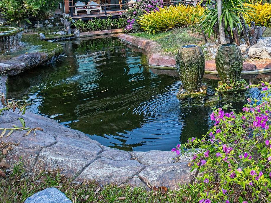 There is a pond in the middle of the garden surrounded by flowers.