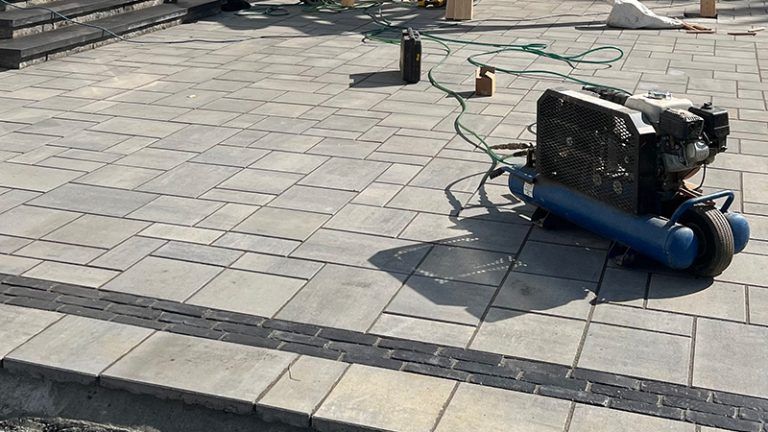 A blue air compressor is sitting on a brick patio.