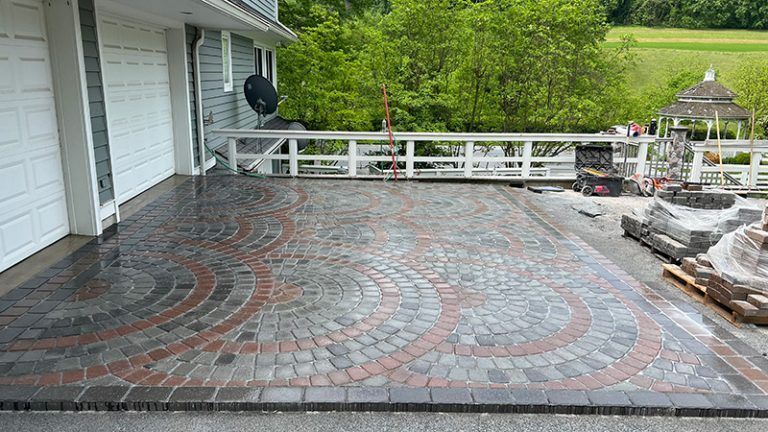 A patio with a gazebo in the background is being built in front of a house.