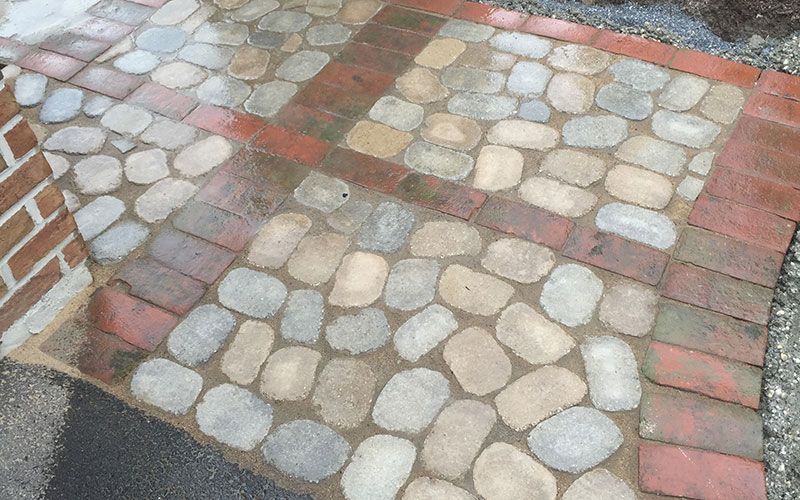 A walkway made of bricks and rocks with a brick wall in the background.