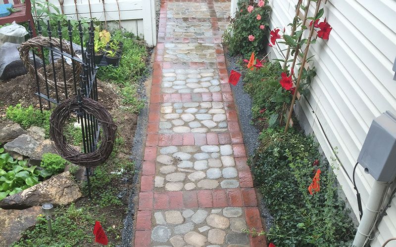 A brick walkway leading to a house with flowers on the side.