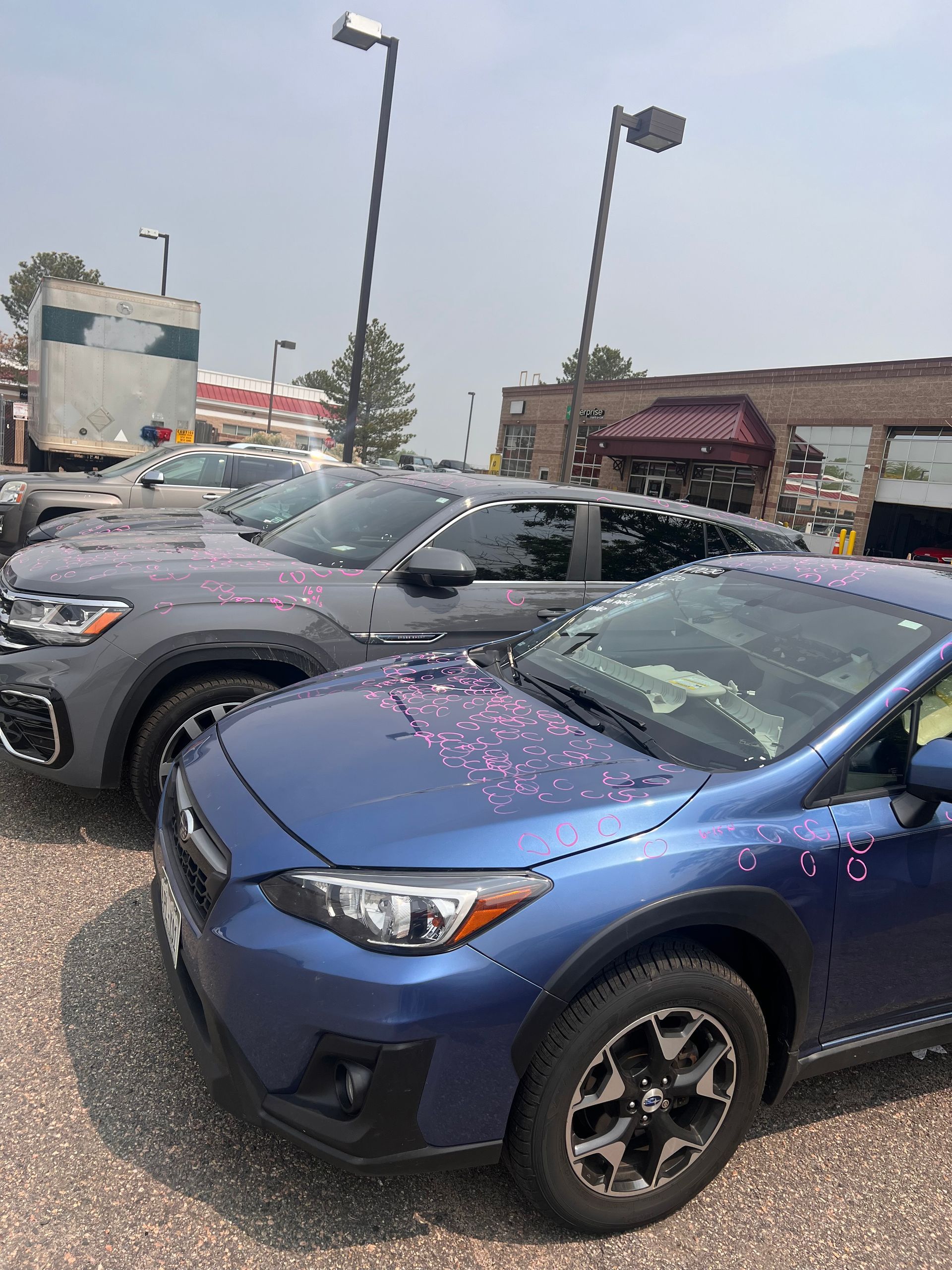 A row of cars are parked in a parking lot in front of a building.
