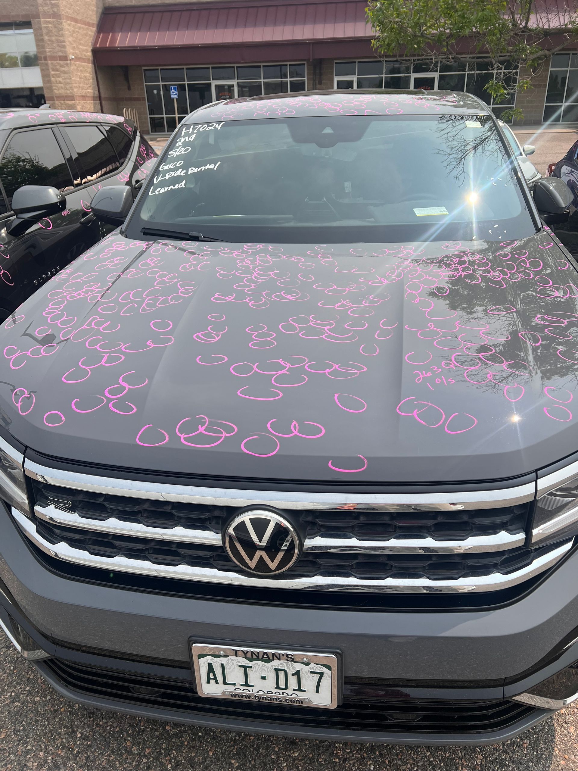 A volkswagen atlas is parked in front of a building with hail damage on the hood.