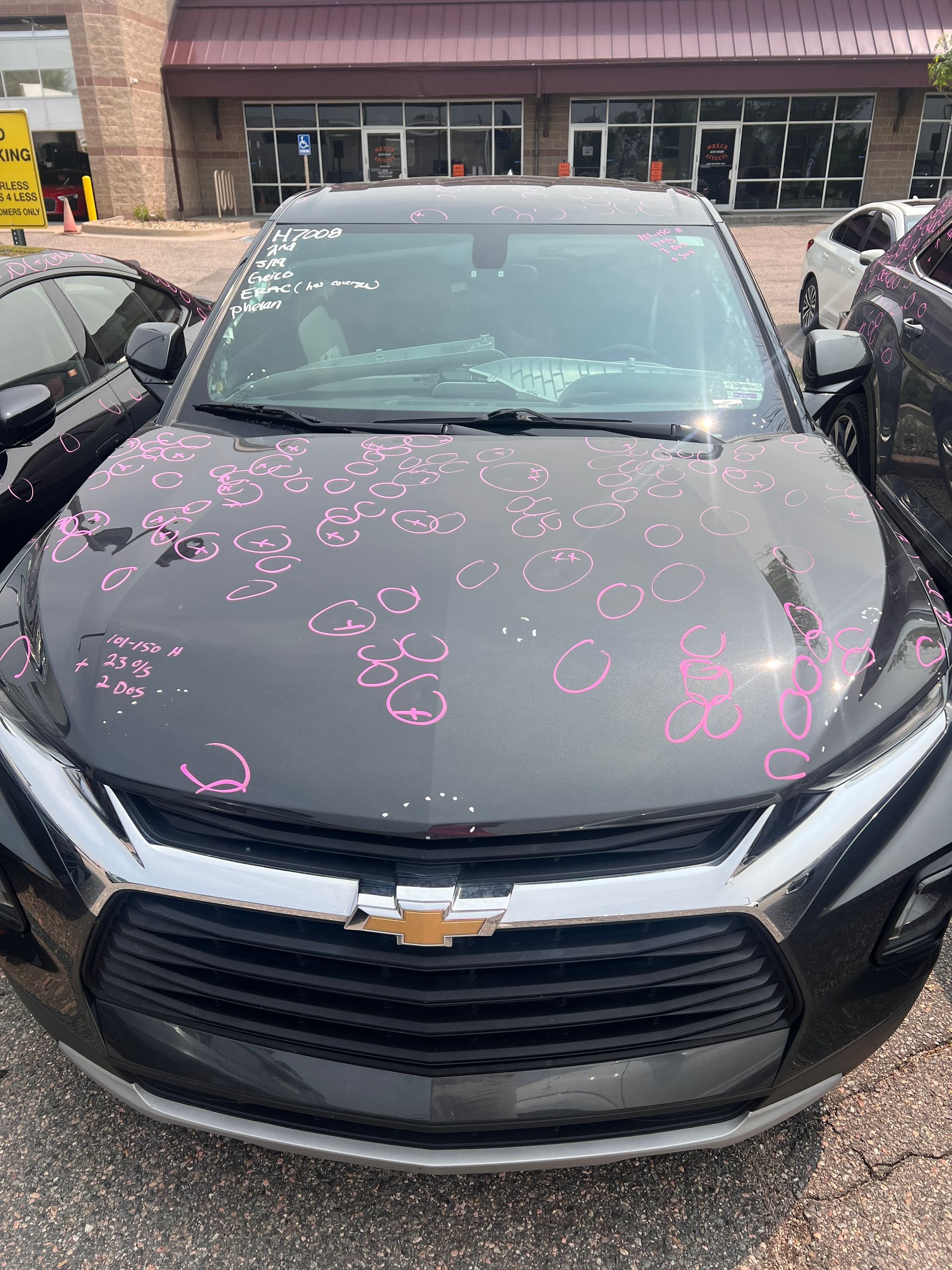 A black car with pink spots on the hood is parked in front of a building.