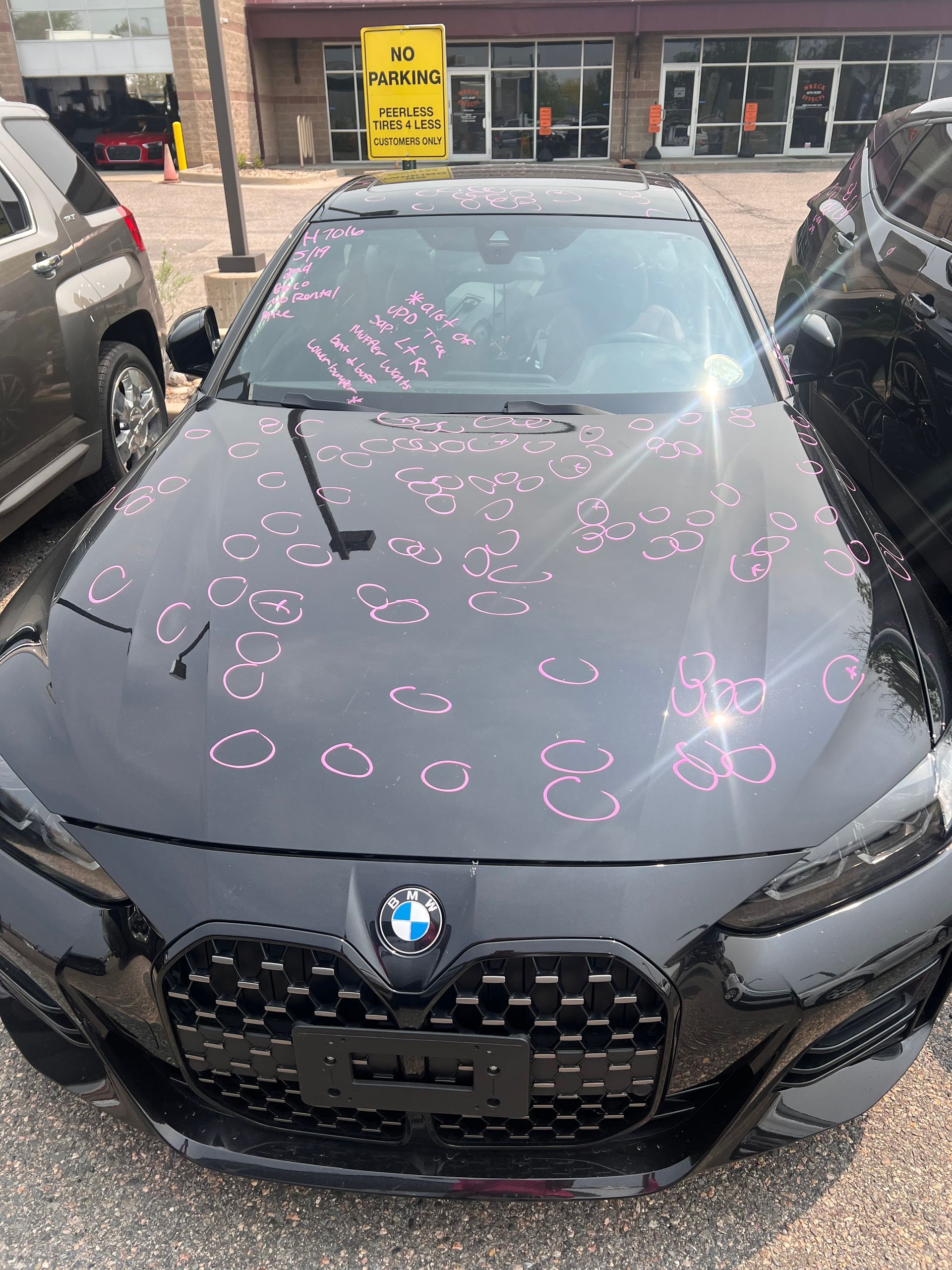 A black bmw with hail damage on the hood is parked in a parking lot.