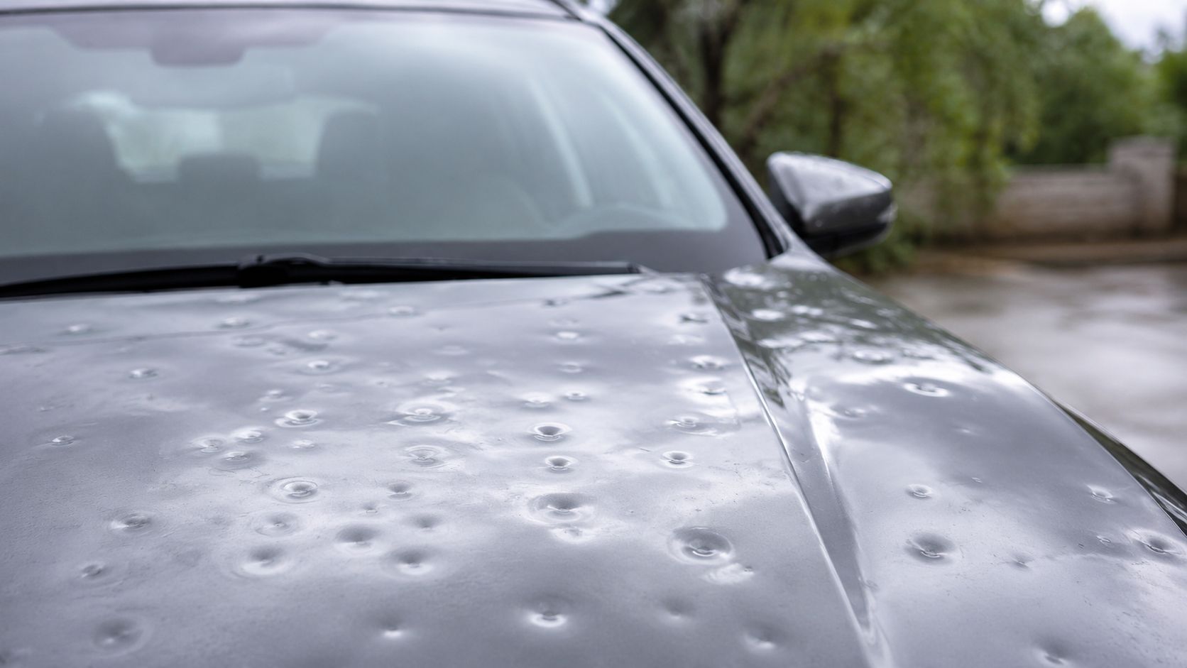 Rain-speckled silver car hood and windshield parked outdoors on a wet day