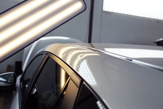 Car roof with glossy metallic paint reflecting overhead lights inside a showroom