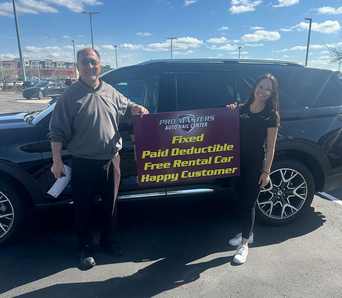 Two people stand by a black SUV holding a sign about paid executive free rental car happy customers.