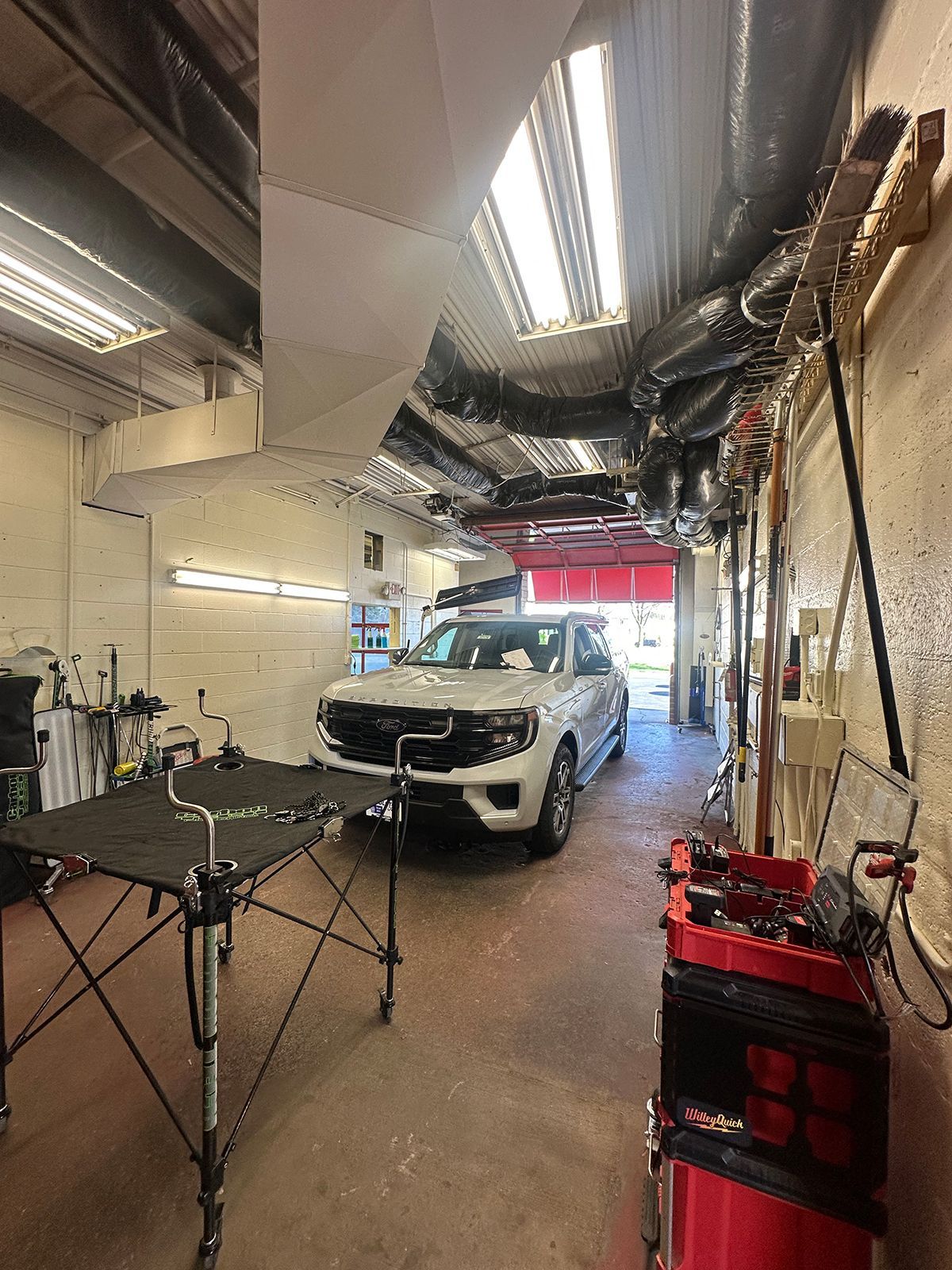 White pickup truck inside an auto repair garage with equipment and lifts nearby